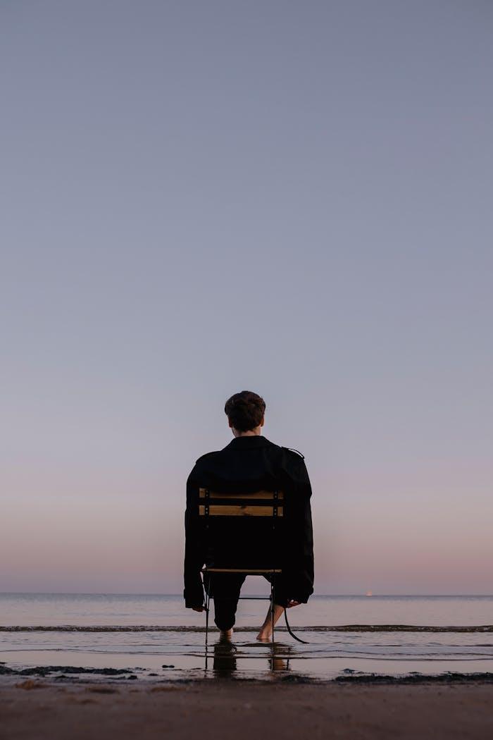 Man Sitting on Chair on Sea Shore at Dusk